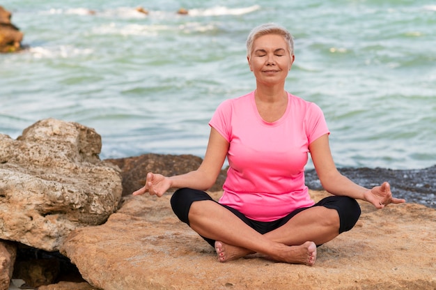 Deportes mujer madura en la playa hacen ejercicios de meditación.