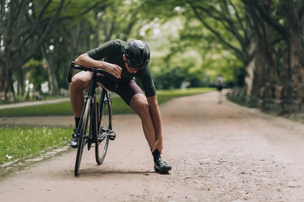 Deportista agotado masajeando las piernas después de andar en bicicleta en el parque