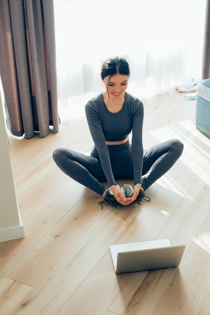 Deportista alegre sonriendo y mirando la pantalla del portátil mientras practica yoga en línea