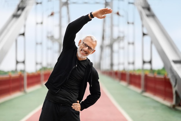 Deportista anciano atlético estirando el cuerpo mientras hace ejercicio al aire libre