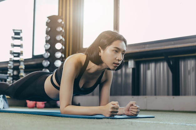 Deportista asiática joven que hace ejercicio del tablón en gimnasio