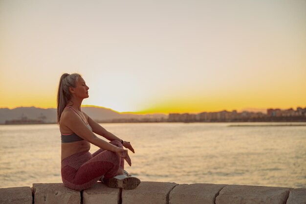 Deportista asiática practicando yoga sentada en el borde a la orilla del mar