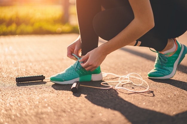 La deportista se ata los cordones de los zapatos y se prepara para hacer ejercicios cardiovasculares con saltar la cuerda al aire libre