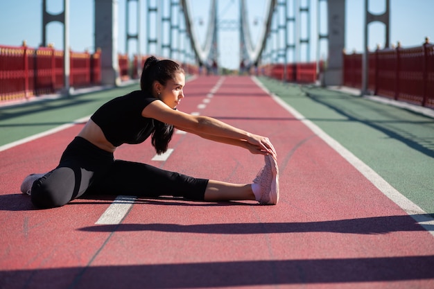 Deportista atractiva haciendo estiramientos y preparándose para correr en el puente. Espacio para texto