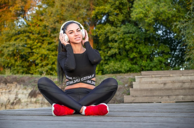 La deportista y los auriculares escuchan música y sonríen./Niña - amante de la música con auriculares al aire libre disfrutando de la música.