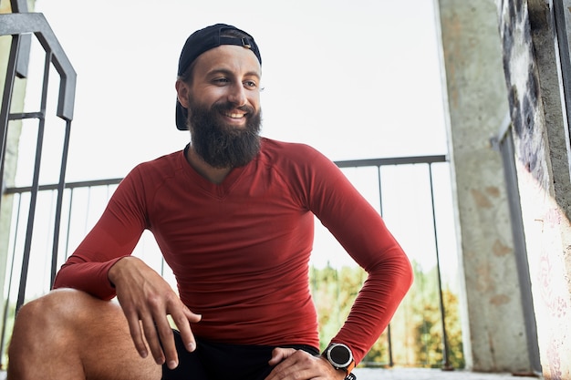 Foto deportista barbudo smilling activo descansar y sentarse en las escaleras en un día brillante