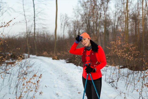 Foto deportista con bastones de trekking tomando un descanso del nórdico corriendo en el bosque en un frío día de invierno