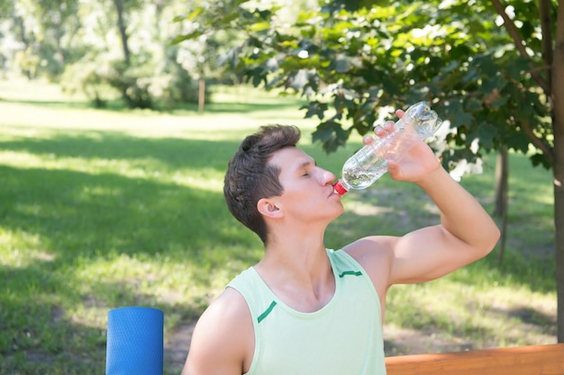 Deportista bebe agua en el parque en un día soleado