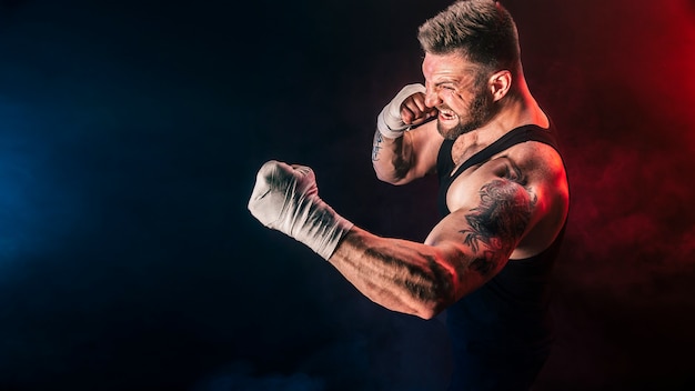 Foto deportista boxeador de muay thai peleando sobre fondo negro con humo.