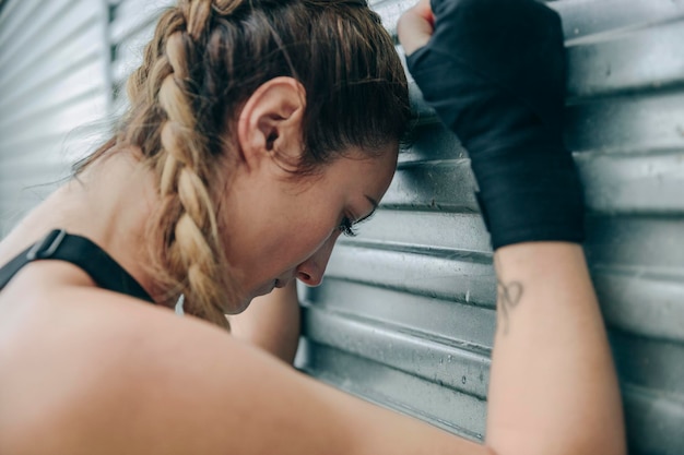 Deportista cansada descansando apoyada en una pared de metal al aire libre