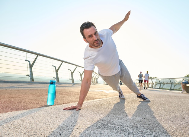 Deportista caucásico de mediana edad haciendo flexiones haciendo ejercicio en el puente de la ciudad de cristal al amanecer Botella con agua en la cinta de correr Deporte concepto de estilo de vida activo y saludable