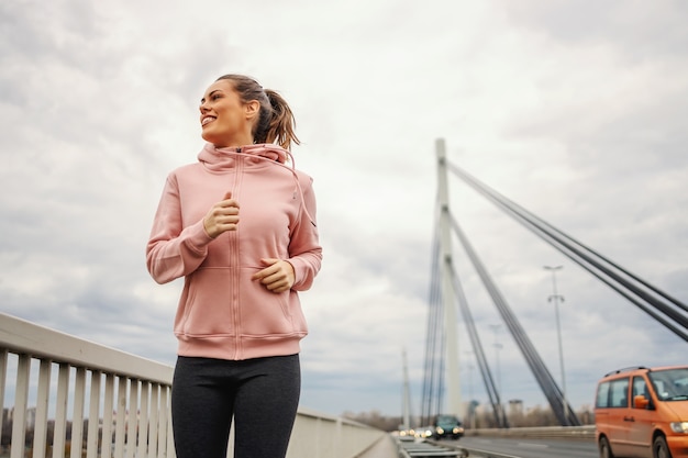 Deportista en chándal para correr en el puente en tiempo nublado. Concepto de estilo de vida saludable.