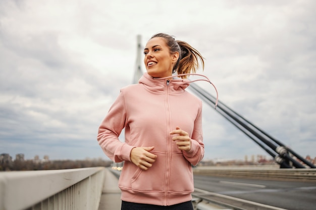 Deportista en chándal para correr en el puente en tiempo nublado. Concepto de estilo de vida saludable.