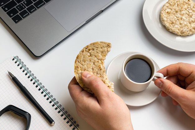 Deportista comiendo rondas de arroz crujientes con cacahuetes, taza de café cerca de la computadora portátil