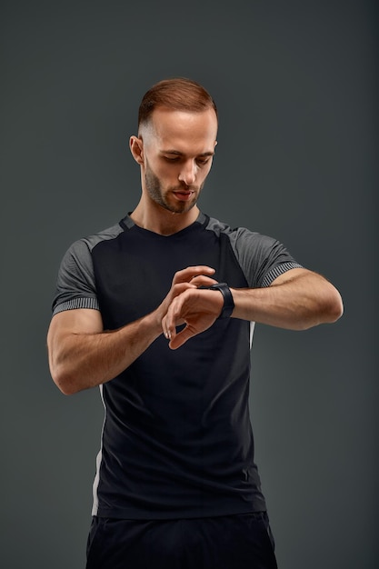 Deportista comprobando la frecuencia cardíaca en el rastreador de fitness cuando se entrena en estudio con fondo gris