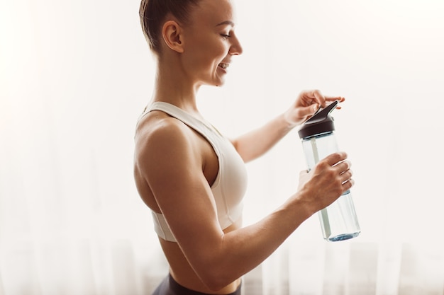 Deportista de cultivo con botella de agua en casa