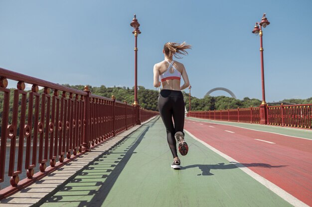 Deportista delgada corre a lo largo de la formación de la pasarela en un día soleado de verano