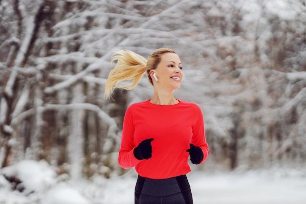 Deportista delgada corriendo en el bosque en el día nevado de invierno. Fitness de invierno, clima nevado, vida saludable