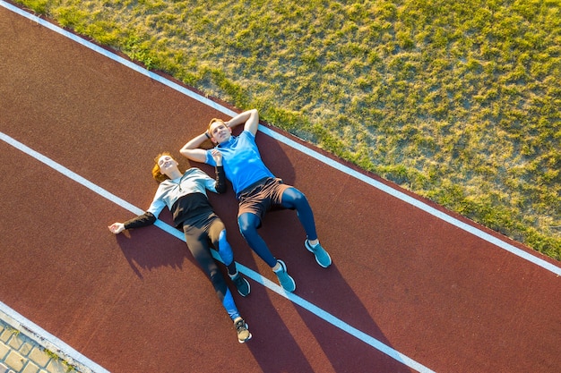 Deportista y deportista recostada sobre la pista de goma roja de un estadio