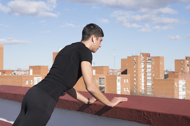 Deportista deportivo fuerte en ropa deportiva entrenamiento de calentamiento hacer ejercicio de estiramiento en un techo escuchando
