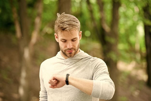 Deportista entrenando con un dispositivo de podómetro Atleta de hombre en la cara ocupada verifica el fondo de la naturaleza del rastreador de ejercicios Atleta con cerdas con rastreador de ejercicios o podómetro Concepto de dispositivo deportivo