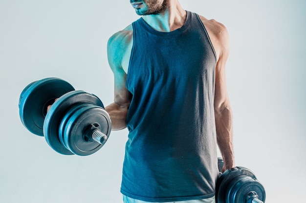 Deportista entrenando los músculos bíceps con mancuernas. Hombre barbudo usar uniforme deportivo. Aislado sobre fondo turquesa. Sesión de estudio