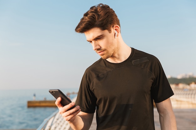 Deportista escuchando música con auriculares mediante teléfono móvil.