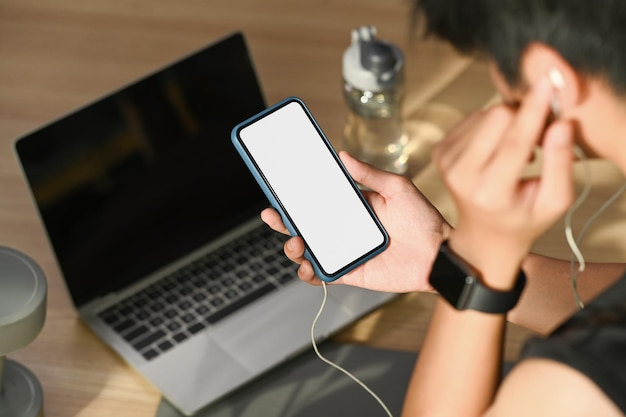 Deportista escuchando música con auriculares y usando el teléfono móvil preparándose para hacer ejercicio en casa