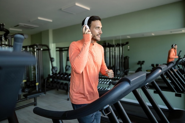 Deportista feliz escuchando música en los auriculares mientras corre en una caminadora