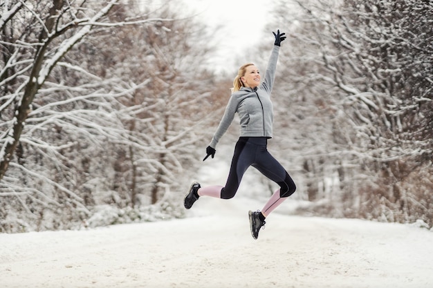 Deportista feliz saltando en camino cubierto de nieve en invierno. Vida sana, deporte de invierno, libertad