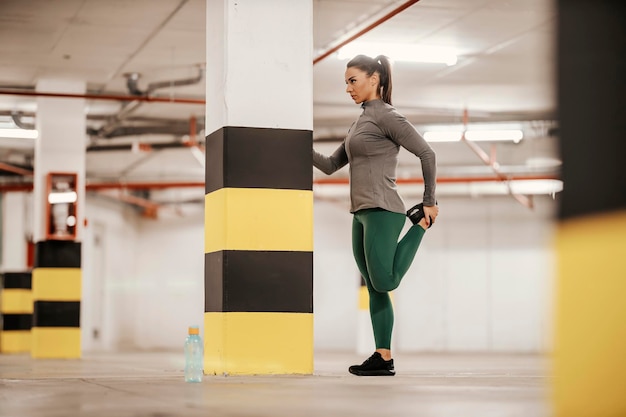 Una deportista en forma está estirando la pierna y haciendo ejercicio en el garaje subterráneo