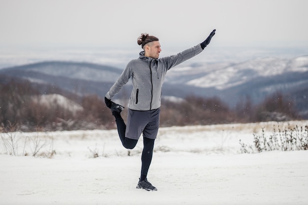 Deportista en forma haciendo ejercicios de estiramiento en la naturaleza en un día nevado de invierno. Hábitos saludables, fitness al aire libre, fitness de invierno