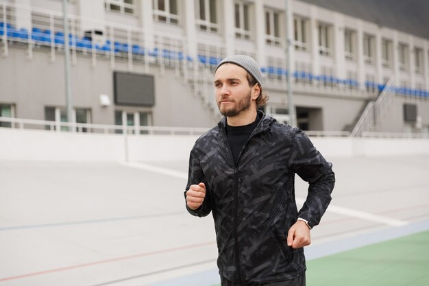 Deportista en forma joven confiado que se ejecuta en la pista de carreras en el estadio al aire libre