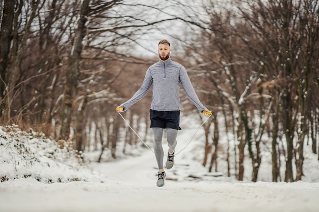 Deportista en forma de saltar la cuerda en la naturaleza sobre la nieve en invierno. Fitness de invierno, hábitos saludables, clima frío