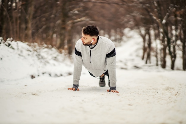 Deportista fuerte haciendo flexiones en la naturaleza en camino nevado en invierno. Estilo de vida saludable, fitness de invierno, ejercicios de fuerza.