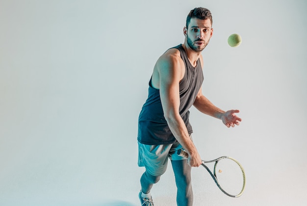 Deportista golpeando la pelota de tenis con raqueta. El joven tenista europeo barbudo se centra en el juego. Aislado sobre fondo turquesa. Sesión de estudio. Copia espacio