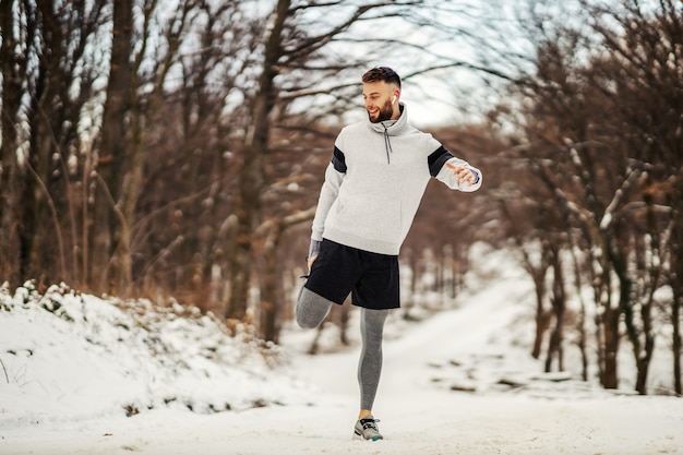 Deportista haciendo ejercicios de estiramiento y preparándose para correr en la naturaleza en un día nevado de invierno. Fitness de invierno, deporte, clima frío