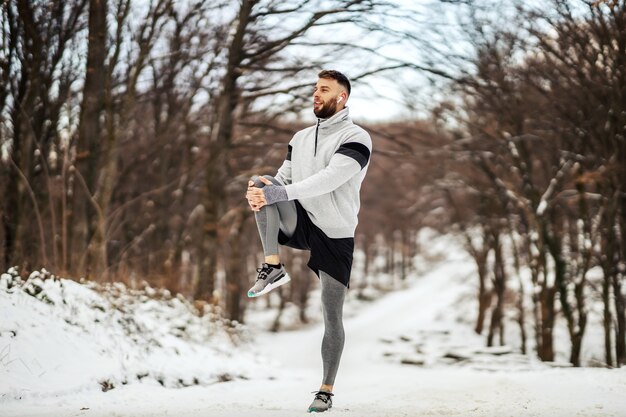 Deportista haciendo ejercicios de estiramiento y preparándose para correr en la naturaleza en un día nevado de invierno. Fitness de invierno, deporte, clima frío