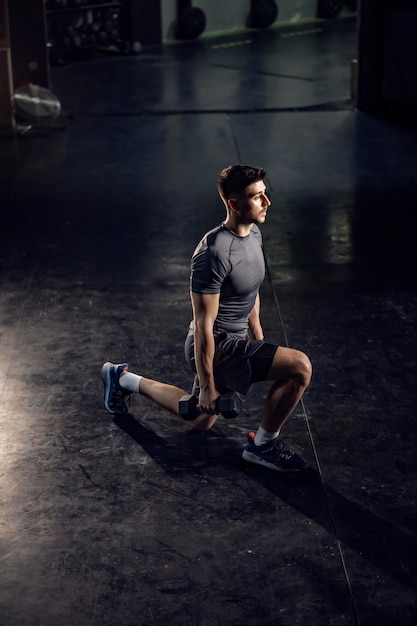 Un deportista haciendo estocadas con pesas en un gimnasio.