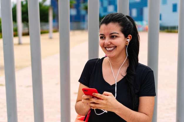 Deportista hispana de pie en un parque comprobando su teléfono celular