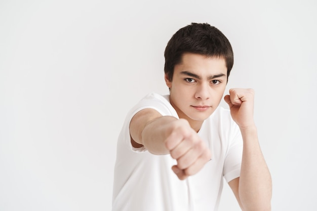 Deportista joven confidente que hace ejercicios de boxeo aislado sobre la pared blanca