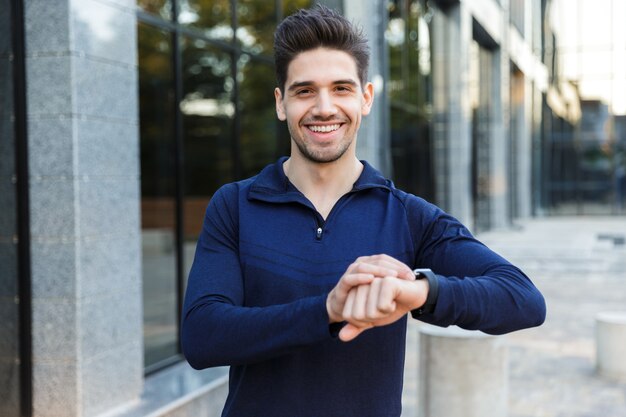 Deportista joven guapo de pie al aire libre, control de tiempo