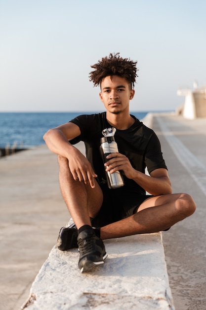 Deportista joven guapo sentado al aire libre en la playa de agua potable