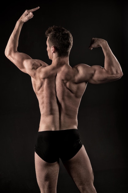 Deportista con manos fuertes, bíceps, tríceps. Atleta hombre con cuerpo musculoso, torso, vista posterior. Pose de culturista sobre fondo oscuro. Poder, salud, bienestar, cuidado corporal, vintage, retro, dieta