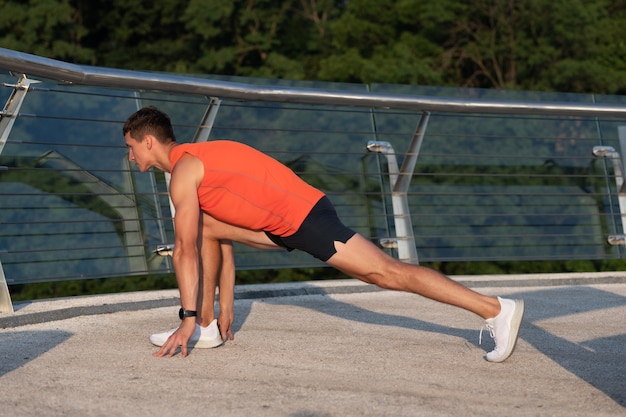 El deportista mantiene la posición de estocada haciendo una rutina de estiramiento después de un entrenamiento atlético al aire libre en el paseo marítimo, estirando.