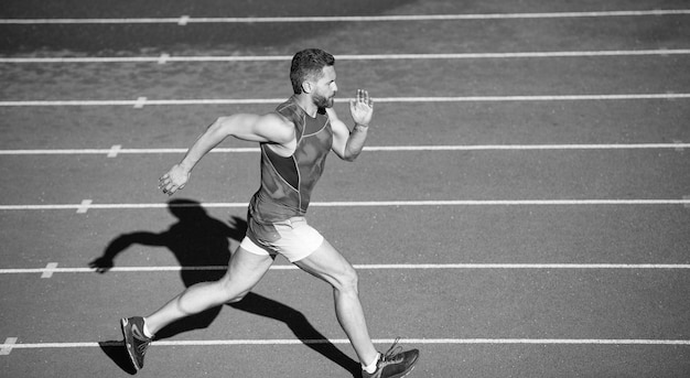 Deportista masculino en ropa deportiva corre rápido corriendo en la distancia de la pista de atletismo