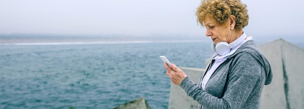 Deportista mayor que mira su smartphone por el embarcadero del mar