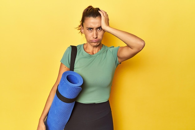 Deportista de mediana edad con estera de yoga en un estudio amarillo sorprendida