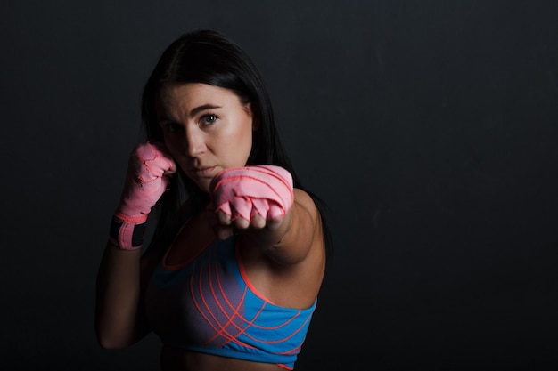 Deportista muay thai mujer boxeadora posando en el estudio de entrenamiento en fondo negro