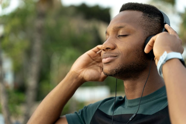 Deportista multirracial con auriculares escuchando música con los ojos cerrados cerca del mar